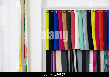 Rangées d'échantillons de textiles colorés accrochés sur un mur blanc avec de longs rubans de mesure dans un atelier de couture moderne et léger avec équipement spécial Banque D'Images