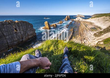Bas section de randonneur mâle assis sur la falaise appréciant la vue de la mer contre le ciel Banque D'Images