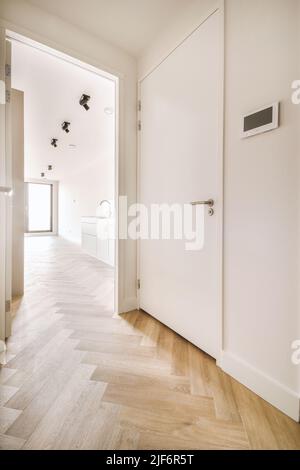 Couloir étroit et lumineux avec de nombreuses portes aux murs blancs et une lampe au-dessus du sol en bois Banque D'Images