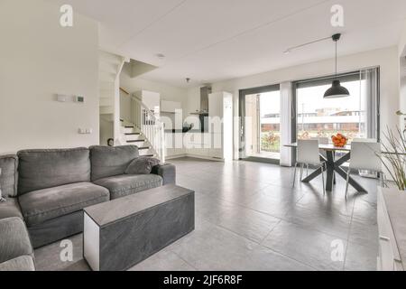 Confortable canapé gris et table basse dans ce studio spacieux avec cuisine et coin repas à la lumière du jour Banque D'Images