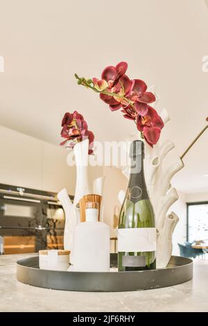Bouteille de boisson alcoolisée servie sur un plateau avec des fleurs d'orchidées dans des vases et placée sur une table dans une cuisine légère dans un appartement moderne Banque D'Images