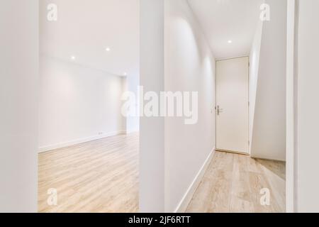 Couloir étroit avec murs et portes blancs menant à une chambre spacieuse avec fenêtres et parquet dans un appartement moderne Banque D'Images