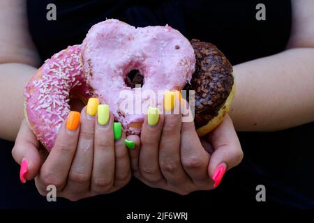 femme avec des extensions d'ongle peintes dans la variété de couleurs tenant des beignets glacés Banque D'Images