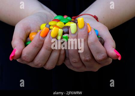 femme avec des extensions d'ongle peintes dans une variété de couleurs tenant des bonbons colorés Banque D'Images