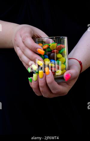 femme avec des extensions d'ongle peintes dans une variété de couleurs tenant le verre rempli de bonbons colorés Banque D'Images