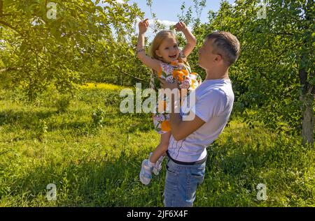 Bonne petite fille dans les bras de son père. La fille joue et rit dans la nature. Le jour du père, papa tenant joyeuse fille souriante dans ses bras parmi les Banque D'Images