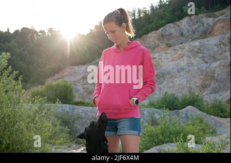 Une femme propriétaire de chien debout dans une belle nature au lever du soleil avec lui fidèle Labrador noir retriever regardant son observation dans les yeux des autres. Banque D'Images