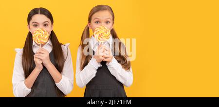 Les enfants affamés tiennent des sucettes spiralées colorées sur fond jaune de bâtons. Adolescent avec bonbons, affiche en-tête de bannière, espace de copie. Banque D'Images