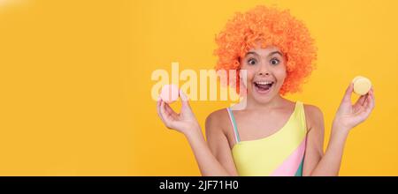 dent douce. drôle enfant dans la perruque clown tient macaron français. enfant étonnant vêtements de bain. Adolescent avec bonbons, affiche en-tête de bannière, espace de copie. Banque D'Images