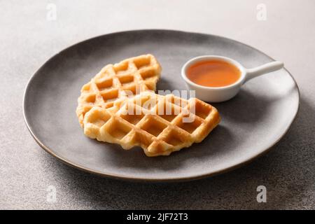 Des croffes virales à la mode dans une assiette servent du sirop d'érable sur fond gris. Croissant comme gaufres. Gros plan. Banque D'Images