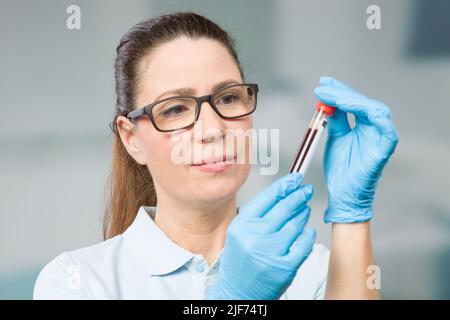 une infirmière ou une scientifique féminine manipule un échantillon de sang dans un tube à essai en laboratoire Banque D'Images