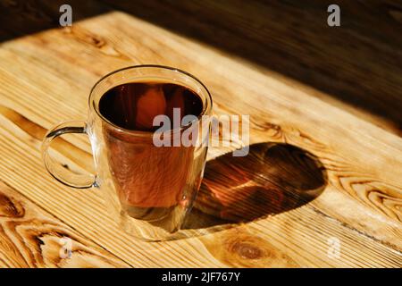 Tasse de thé noir chaud en verre transparent sur table en bois. Banque D'Images