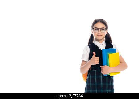 Pupille dans des lunettes tenant des livres et montrant le pouce isolé sur blanc Banque D'Images