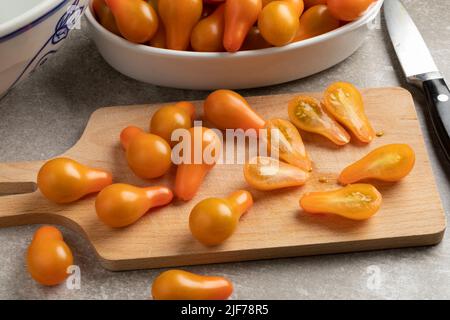 Planche à découper avec tomates poire entières jaunes et coupées en deux gros plan dans la cuisine Banque D'Images