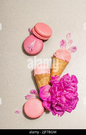 Gaufres à la crème glacée avec macarons sur fond de pierre. Dessert sucré, pétales de fleurs de pivoines, concept d'été. Style romantique, carte de fête, top vi Banque D'Images