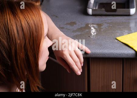 La machine à café est en panne et doit être réparée. La femme essuye les conséquences avec un chiffon. Fuite, déversement de café sur la table de cuisine Banque D'Images