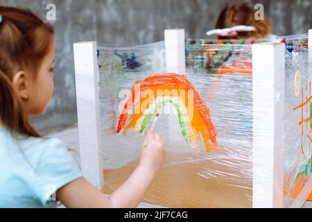 La conduite de cours avec les enfants dans le dessin à la maternelle. Une jeune fille assise et peignant à la main dans un pinceau dans la salle de jeux, près de la vue arrière Banque D'Images