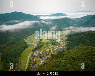 Vue aérienne du brouillard matinal sur un village isolé dans des montagnes boisées Banque D'Images