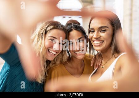 Trois amies multiraciales qui font un geste de cadre de main dans la rue Banque D'Images
