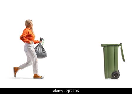 Photo pleine longueur d'une jeune femme transportant un sac de déchets en plastique et se rapprochant d'un bac isolé sur fond blanc Banque D'Images