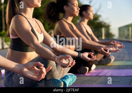 Groupe multi-ethnique de jeunes femmes méditent dans lotus poser au lever du soleil en plein air. Banque D'Images