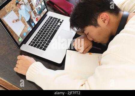 Adolescent asiatique fatigué dormant devant un ordinateur portable pendant une conférence en ligne sur table à la maison Banque D'Images