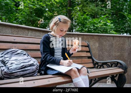 La fille fait ses devoirs et mange un sandwich dans le parc. Banque D'Images