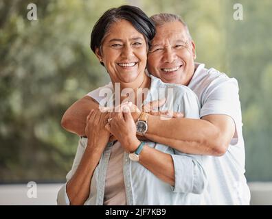Portrait d'un heureux couple senior debout dans le salon montrant de l'affection en embrassant. Un mari et une femme aimant se liant en regardant un appareil photo. L'homme Banque D'Images