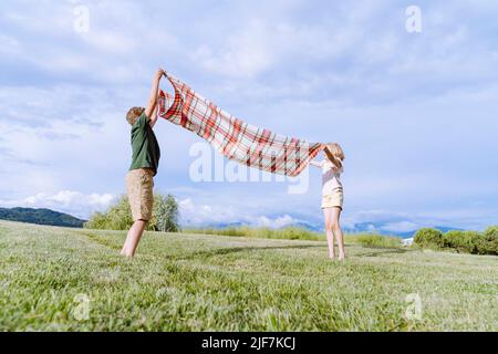 ?hildren pose une couverture de pique-nique dans un champ sur l'herbe. Banque D'Images