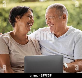 Couple senior en ligne avec un ordinateur portable à la maison, riant et regardant des films. Un week-end de détente pour un couple moderne et âgé. Un homme et une femme heureux Banque D'Images