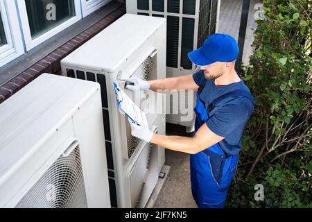 Deux électriciens hommes portant des vestes de sécurité Contrôle de l'unité de climatisation sur le toit du bâtiment Banque D'Images