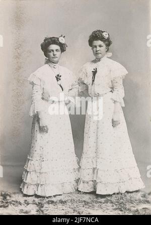 Photographie antique vers 1880 de deux sœurs ou demoiselles d'honneur de Cadillac, Michigan vêtues des meilleures robes florales blanches. SOURCE : CARTE D'ARMOIRE D'ORIGINE Banque D'Images