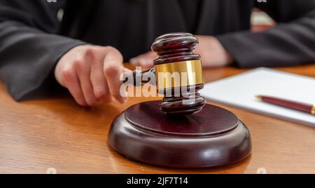 Main féminine tenant une loi de vente aux enchères gavel. Femme juge avec un bloc-notes frappant un maillet en bois, vue rapprochée. Banque D'Images