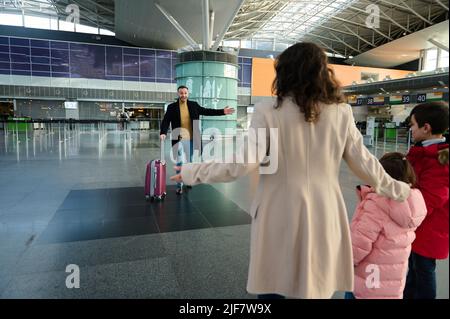 Vue arrière d'une femme avec deux enfants qui rencontre son mari, père à l'aéroport international. La famille tant attendue se réunifier. La réunion attendue depuis longtemps à TH Banque D'Images