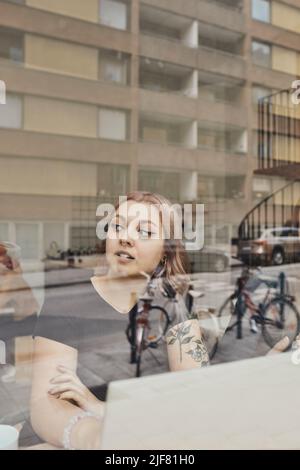 Femme entrepreneure attentionnés qui regarde loin en étant assise dans le bureau, vue à travers la vitre Banque D'Images