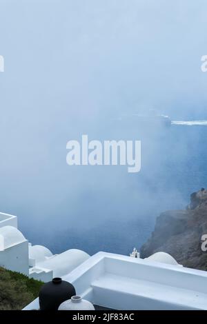 Santorini, Grèce - 13 mai 2021 : le célèbre rocher de Skaros et un ferry approchant l'île de Santorini par temps brumeux Banque D'Images