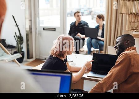 Femme d'affaires expliquant à un collègue un ordinateur portable lorsqu'elle est assise au bureau Banque D'Images