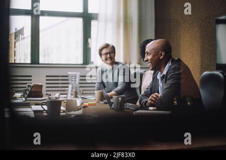 Heureux homme d'affaires mature assis par des collègues à la table de conférence au bureau Banque D'Images