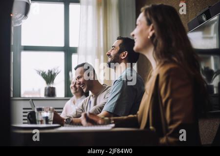 Des hommes d'affaires heureux assis par des collègues à la table de conférence dans le bureau de création Banque D'Images