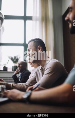 Joyeux homme d'affaires mûr en s'asseyant par des collègues dans la salle de réunion Banque D'Images