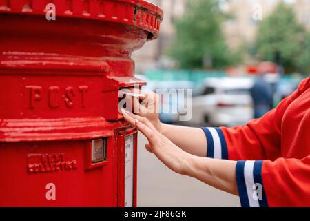 Femme en rouge court poster des lettres dans la boîte rouge en Angleterre Banque D'Images