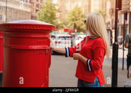 Femme en rouge court poster des lettres dans la boîte rouge en Angleterre Banque D'Images