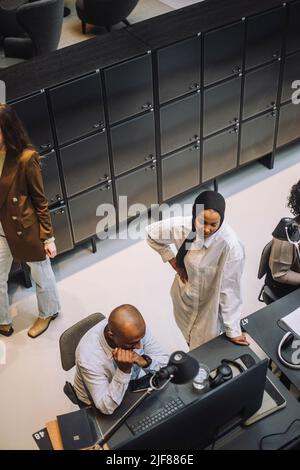 Vue en grand angle d'une jeune femme d'affaires debout à la main sur la hanche discutant avec un collègue assis à son bureau Banque D'Images