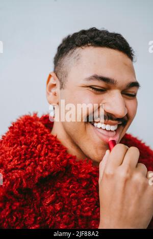 Joyeux gay homme appliquant le rouge à lèvres contre le mur Banque D'Images