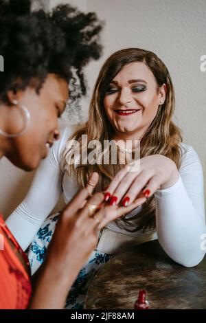 Jeune femme appliquant vernis à ongles à un ami non binaire à la maison Banque D'Images