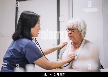 Une travailleuse de la santé examine un patient âgé avec un stéthoscope dans une clinique médicale Banque D'Images