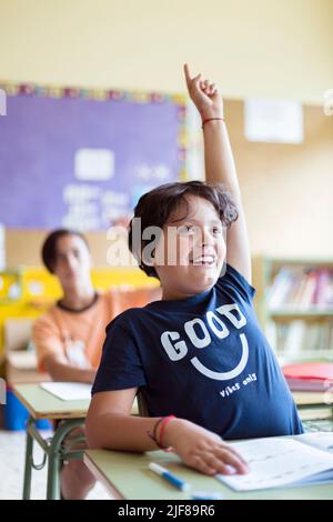 Portrait d'un enfant caucasien souriant avec main levée en classe. Enseignement primaire. Retour à l'école. Banque D'Images