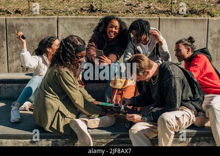 Homme heureux appliquant vernis à ongles sur la main de la femme tout en étant assis par des amis gaies dans le parc Banque D'Images