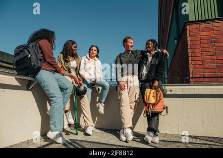 Des amis hommes et femmes parlent les uns avec les autres tout en étant assis sur le mur de soutènement à la terrasse Banque D'Images