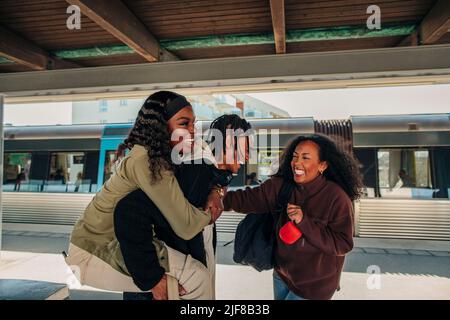Bonne femme debout par un homme coggysoutenant une amie femelle à la plate-forme de la gare Banque D'Images